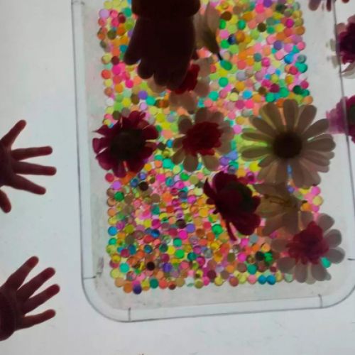 Manos de niños manipulando flores y cuentas de colores en recipiente transparente