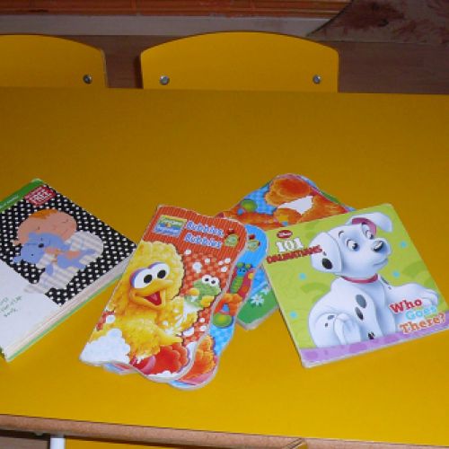 Mesa amarilla con cuatro sillas de niño y cuentos sobre ella