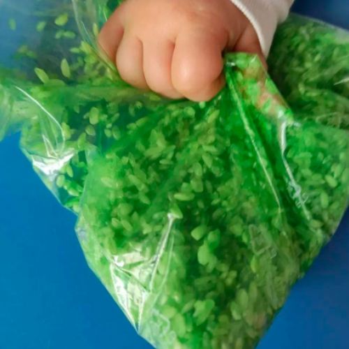 Mano de bebé agarrando paquete de plástico con arroz de color verde dentro